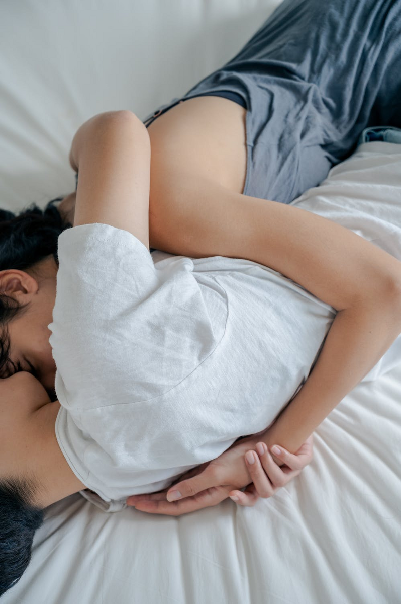 couple cuddling on mattress with white bed sheets