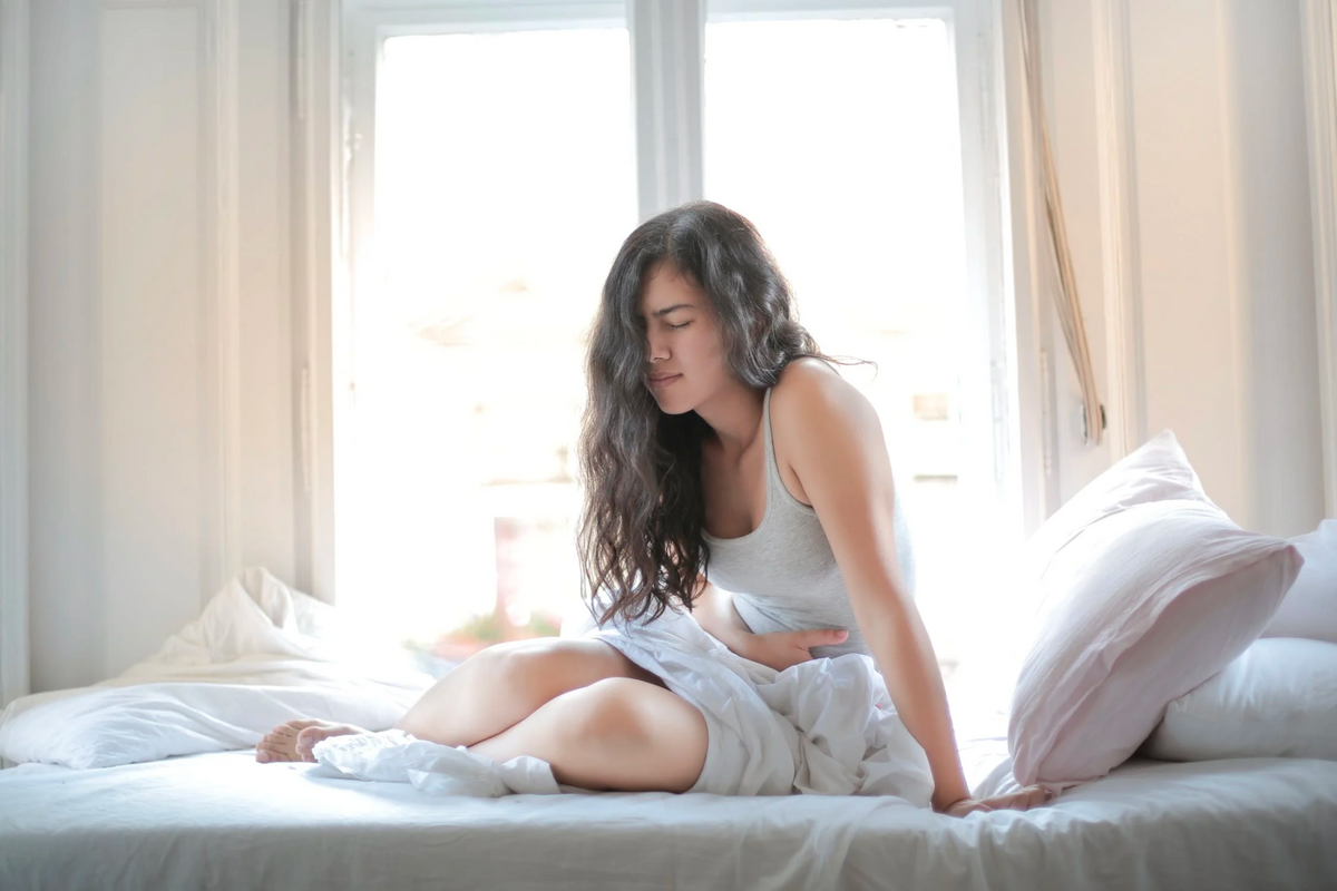 girl holding stomach on mattress looking like she may vomit