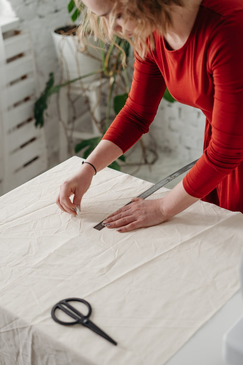 women in red measuring materials to make futon mattress on table