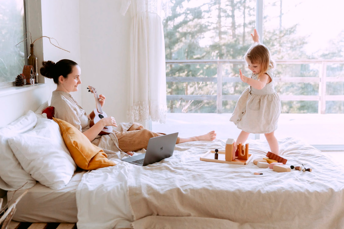 women and her child on a bed with macbook and children's toys